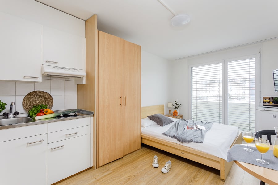 small kitchen area with appliances and utensils, wooden bed, wooden flooring, double window, sink