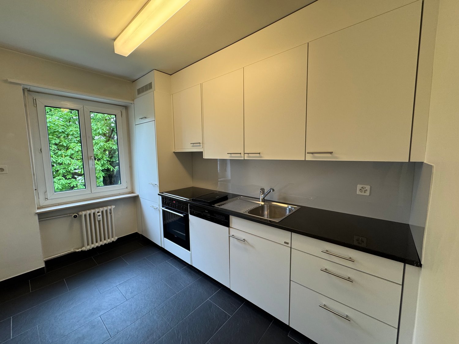 modern kitchen, white cabinets, black countertops, stainless steel sink, oven, dishwasher, window with view