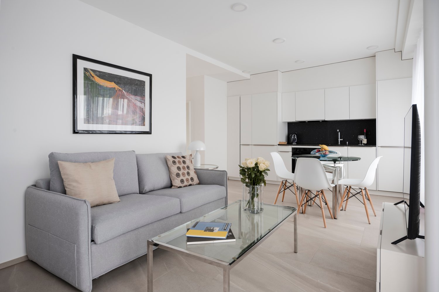 gray sofa, glass coffee table, dining area with table and chairs, kitchen, television, picture frame