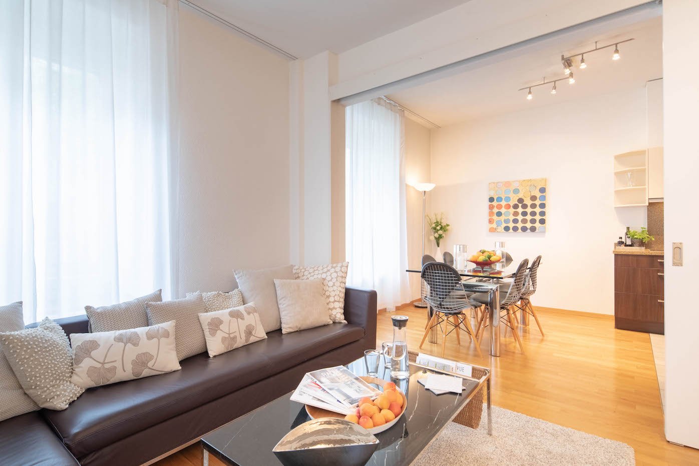 wooden floor, leather sofa, coffee table, dining table with chairs, modern lamps, artwork on the wall