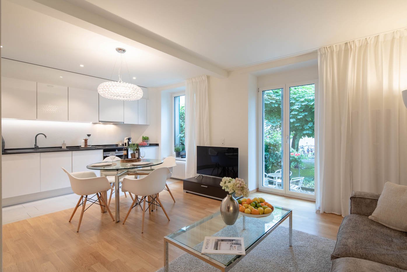 modern apartment, living room, dining area, open kitchen, couch, glass table, glass door leading to terrace, tv, chandelier, white flooring