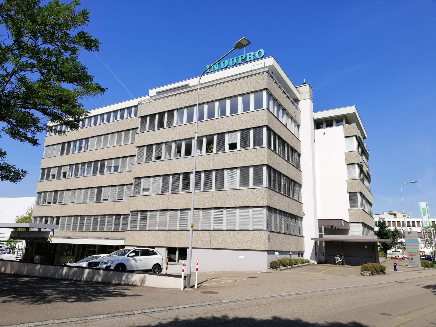 modern office building, multiple floors, glass windows, parking area in front