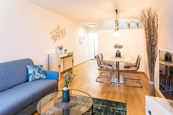 living room with wooden floor, blue couch, glass table, dining table and chairs, plants, wall decorations, lamps
