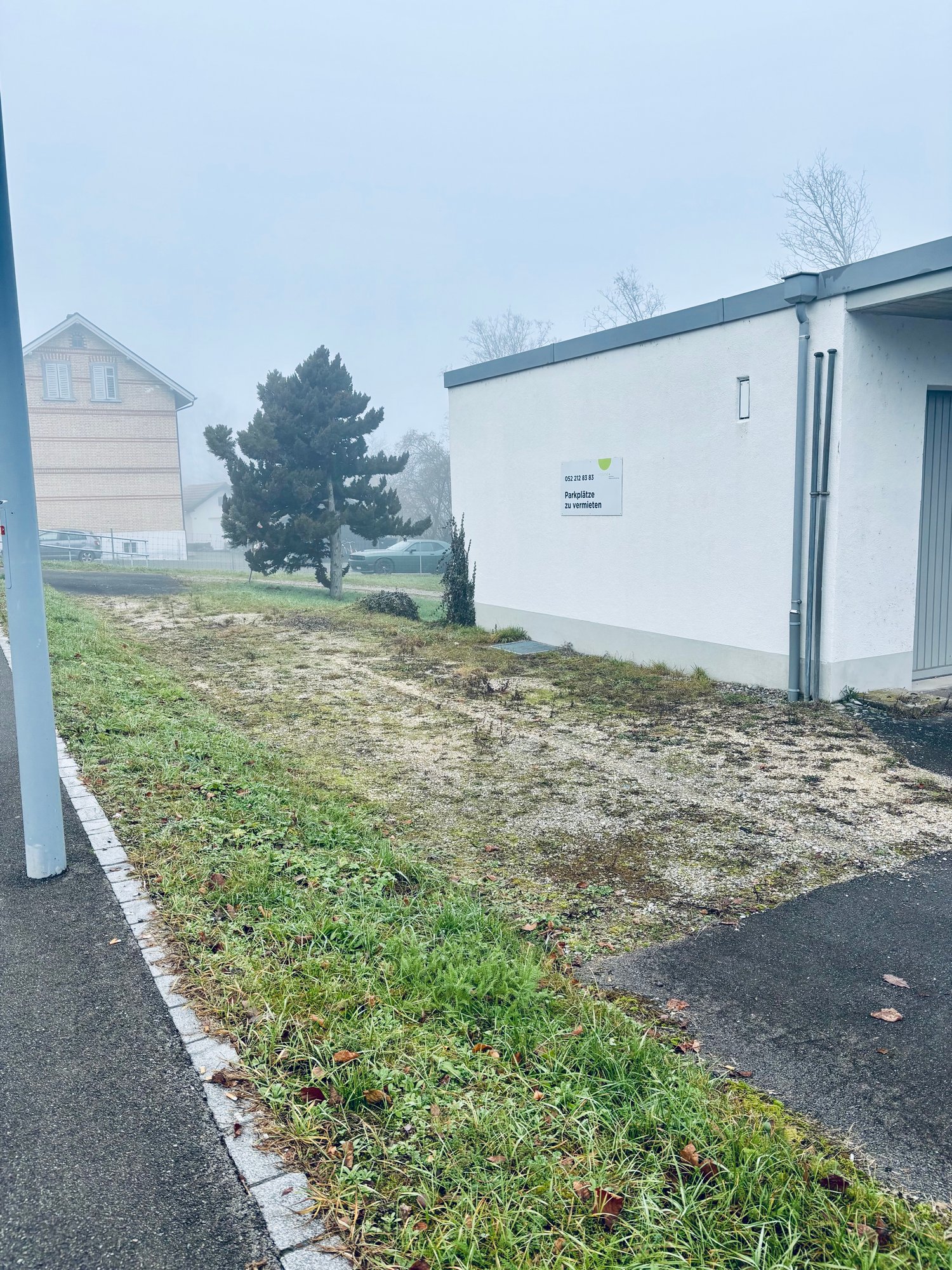 small area with grass, next to a building, car parked in the distance, pathway leading to the building, some dried grass areas