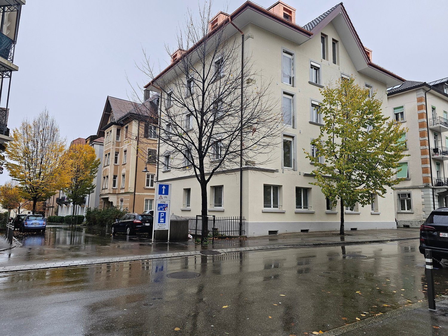 Multi-story apartment building, modern architectural design, concrete structure, multiple windows, parking sign, wet street due to rain