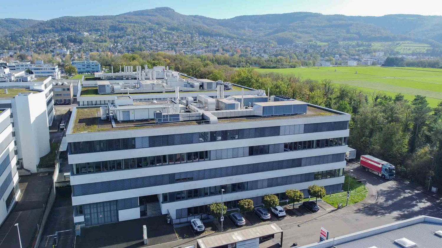 Business building with multiple floors, surrounded by trees, with parking area in front