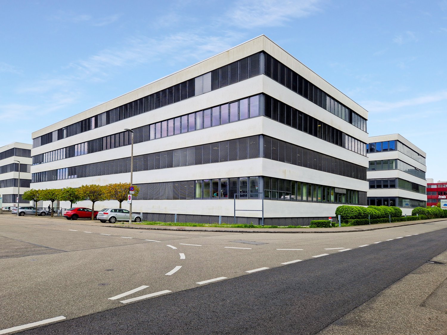 A multi-story office building with glass windows and parked cars