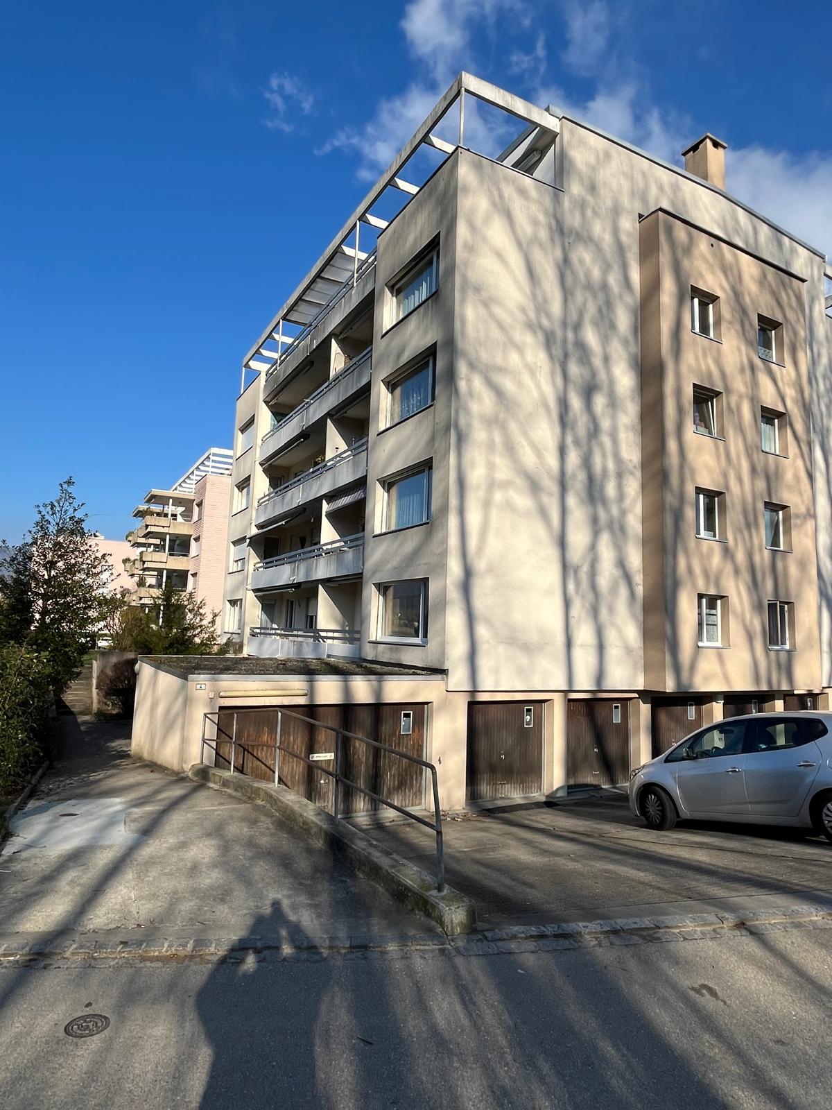 5-story building, beige exterior, multiple balconies, garage entrance, shadow of person and trees