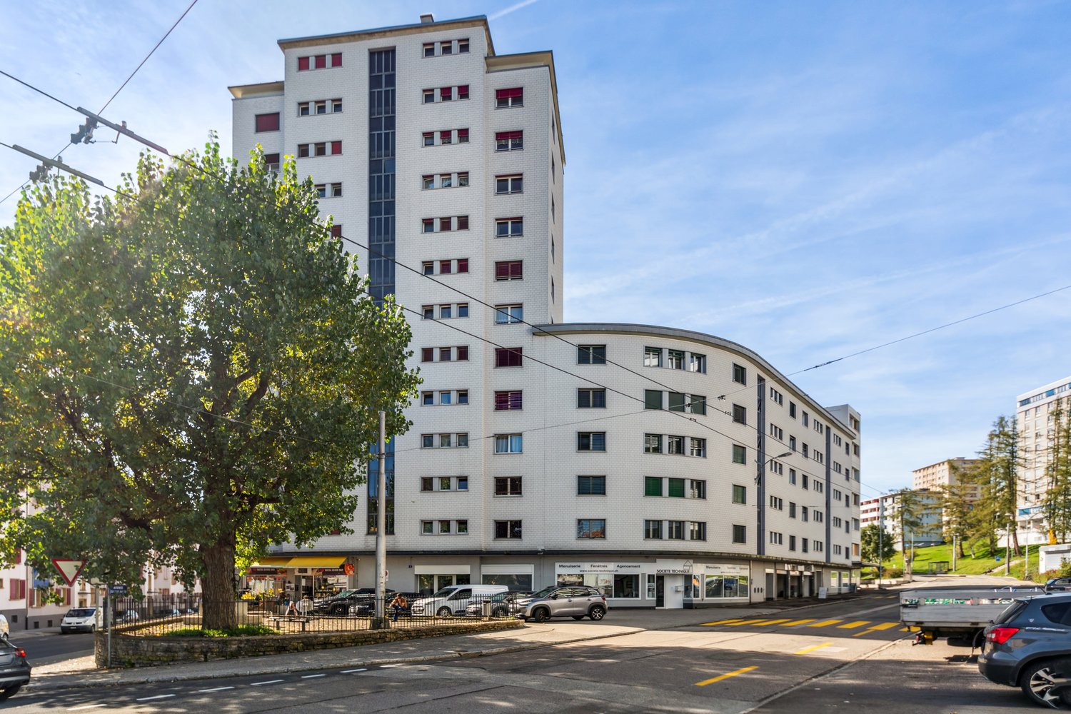 Multi-story building, many windows, yellow storefronts, parked cars, tree, street