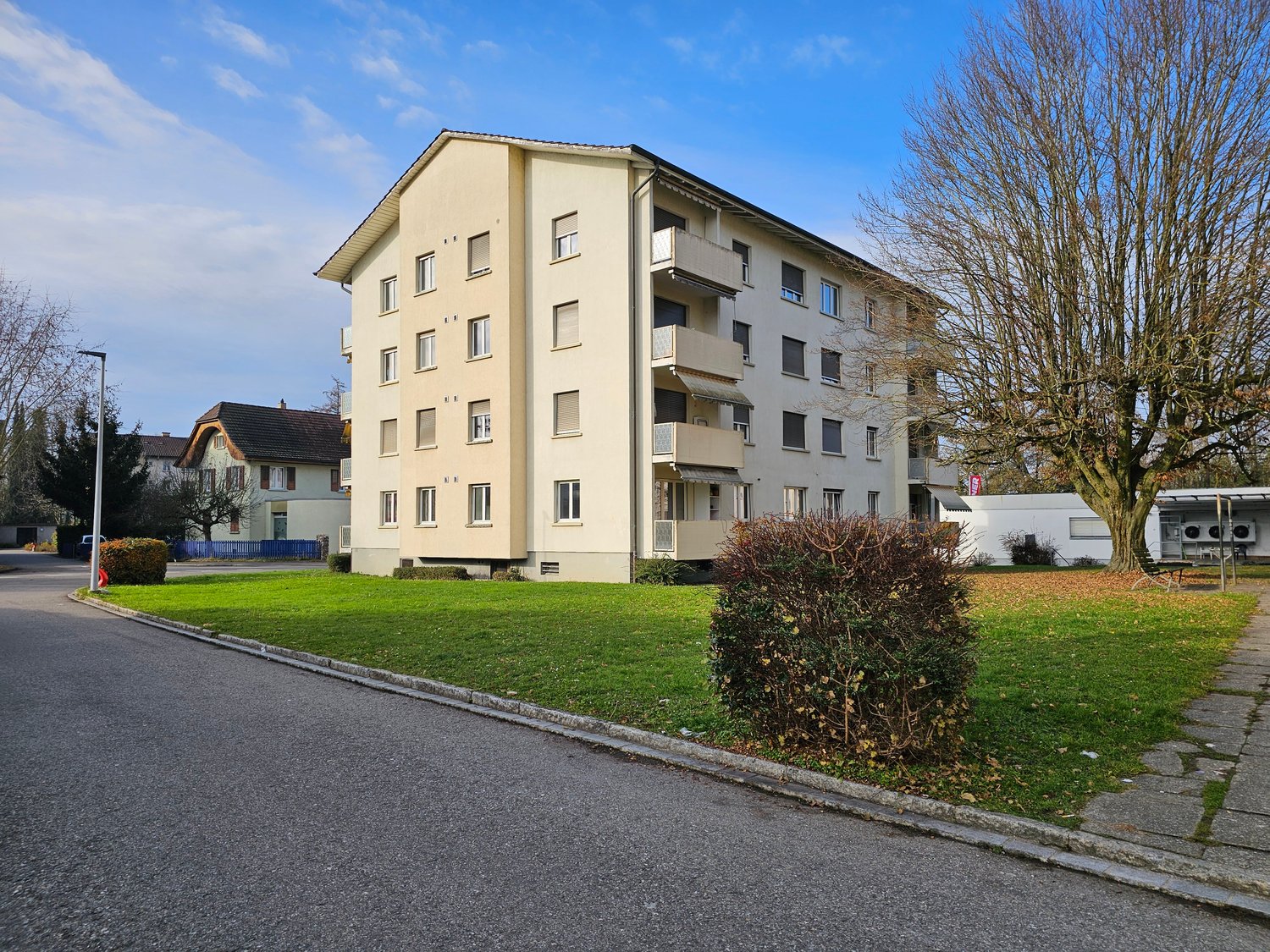 4 story building, beige exterior, balconies, windows, green lawn, street