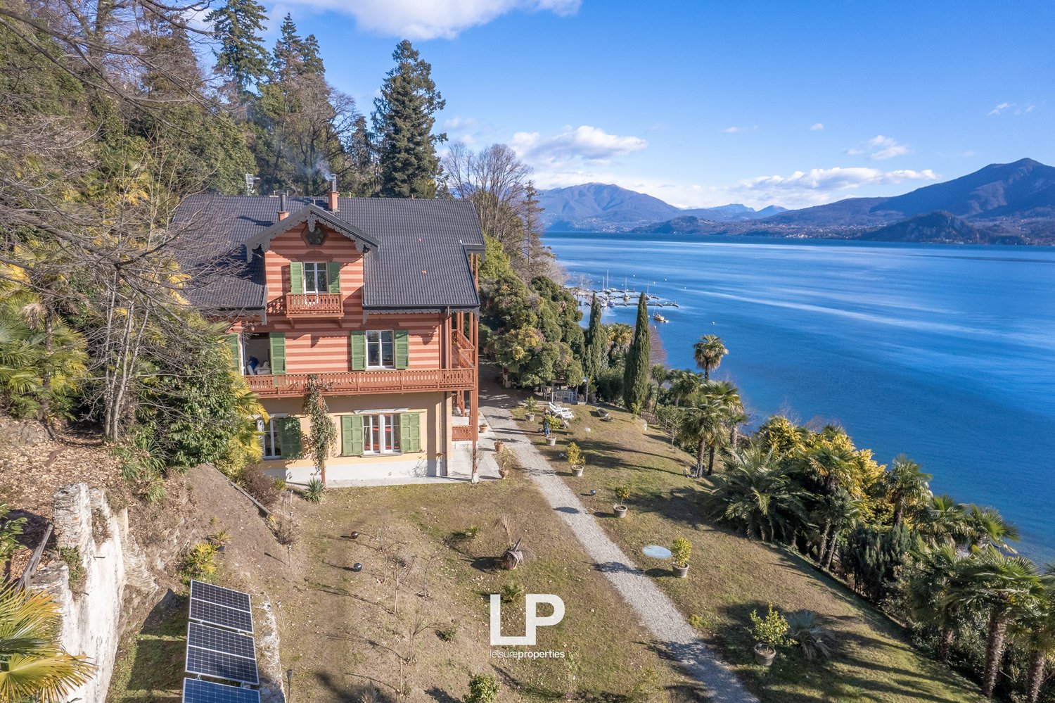 2 story house, red brick, green windows, solar panels, located on a hill, with a sea view