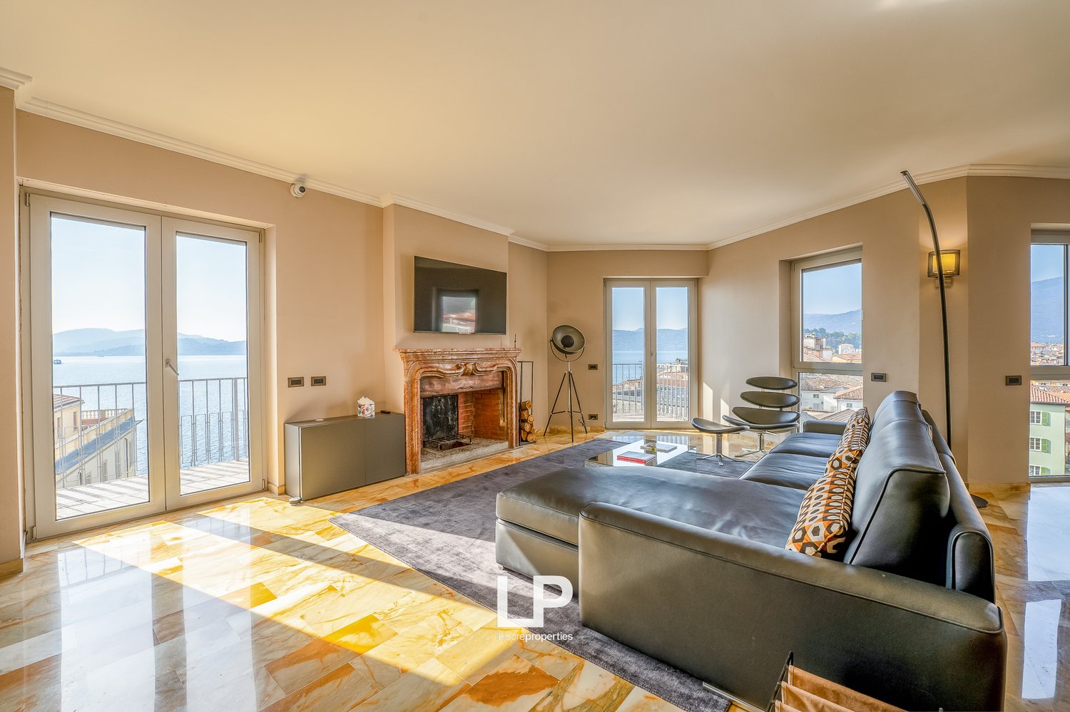 Spacious living room with large windows, balcony, fireplace, leather sofa, and modern decor