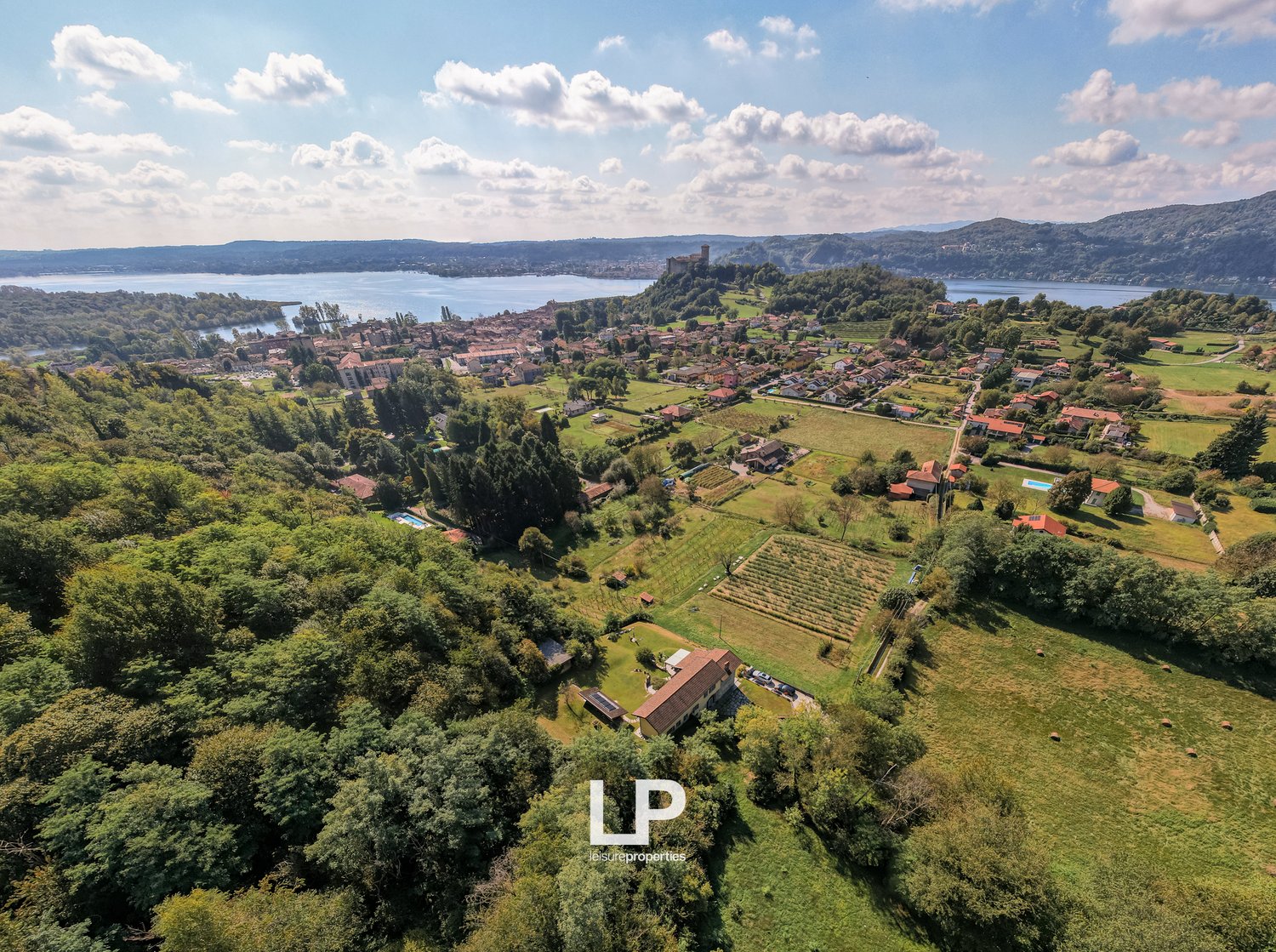 An aerial view of a town with a lake, surrounded by a large garden with a pool and a large house in the center.