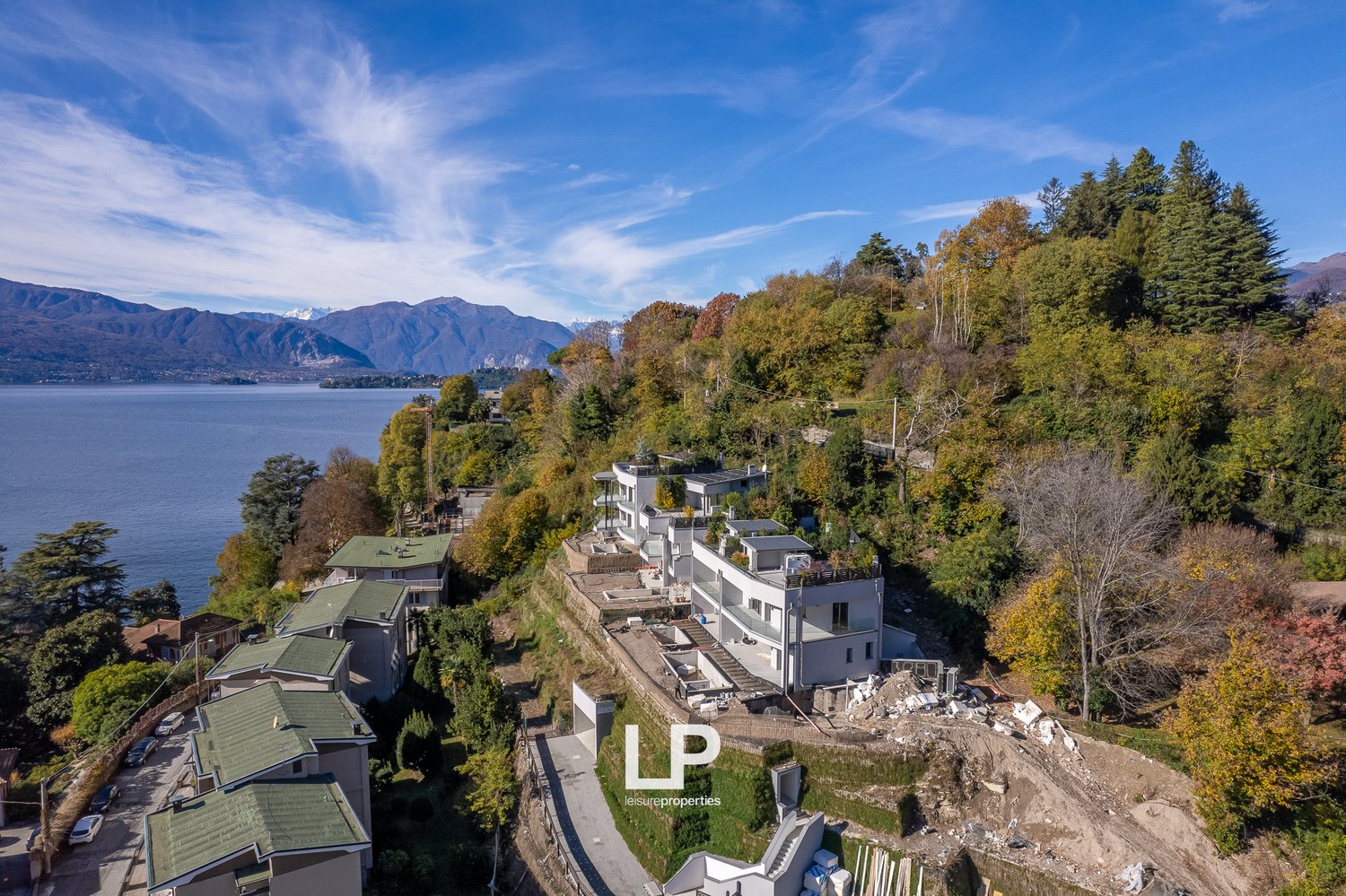 Modern building overlooking a body of water, surrounded by mountains, greenery, and trees.