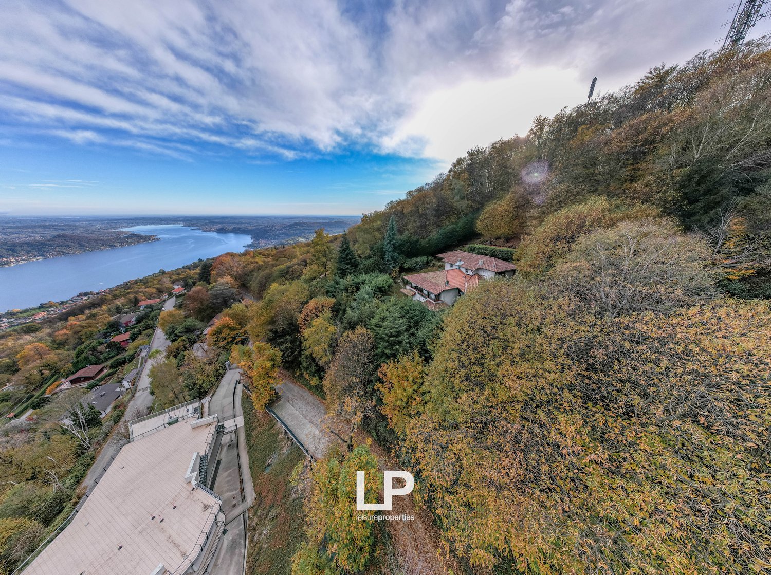 House on hillside, view of lake and city, trees, dirt road, another house in background