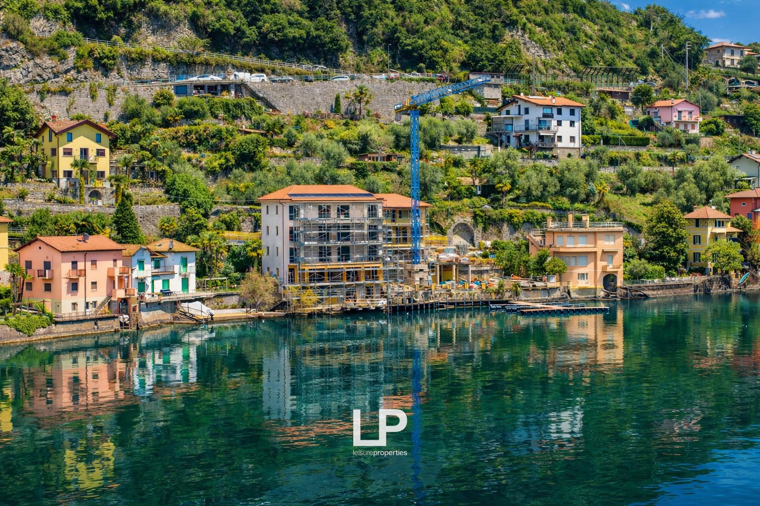 Terraced houses with various architectural designs and colors, under construction buildings, a crane, surrounded by trees and mountains, reflecting on the calm lake