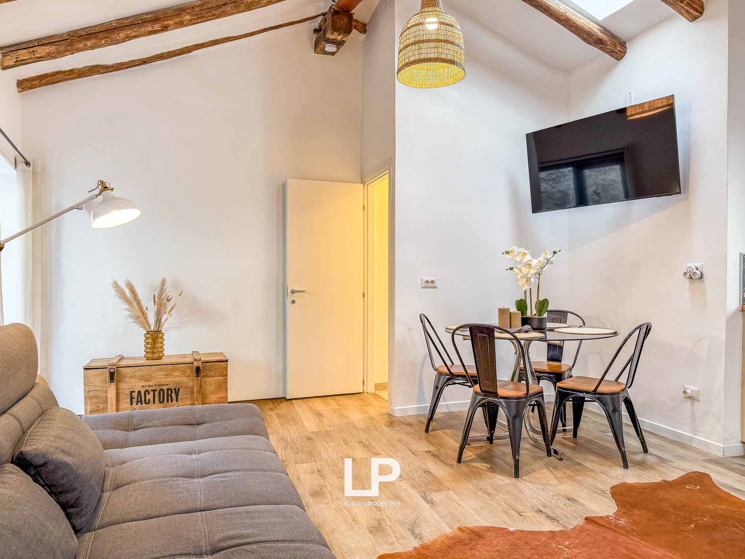 Sofa, dining table with 4 chairs, lamp, TV, wooden floor, wooden beams, wooden box with plant, rug