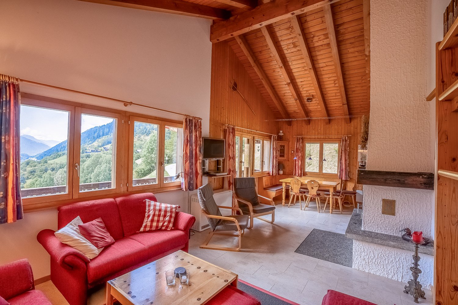 wooden walls and ceiling, fireplace, large windows with mountain views, red sofa, wooden coffee table, dining table and chairs