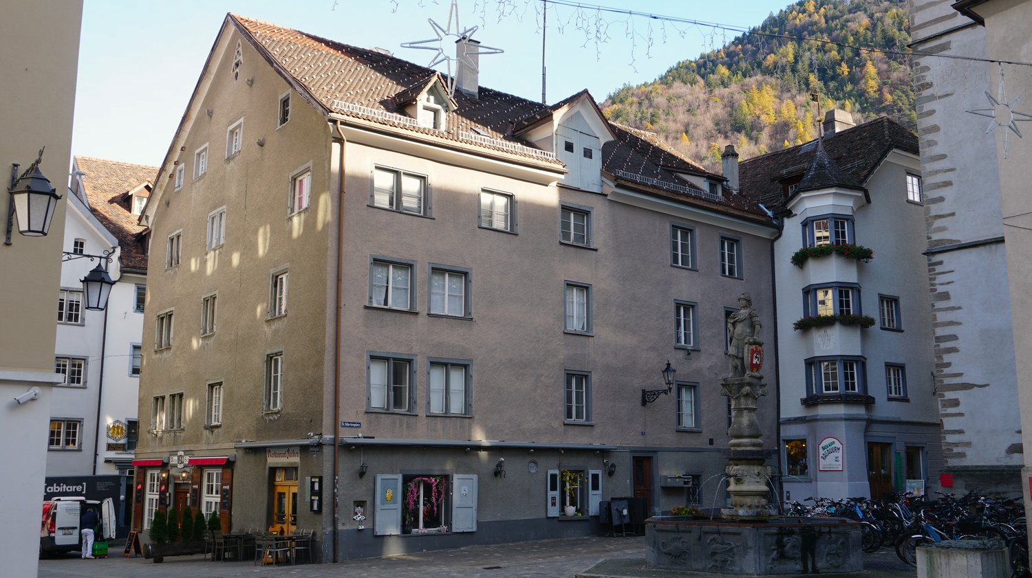 multi-story building with multiple windows, balcony, two floors with shops, statue at the front, bicycles parked in front
