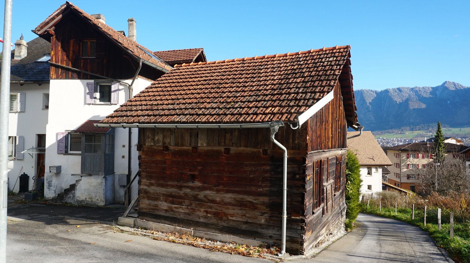 Raised ground floor, wooden walls, terracotta roof, mountains in the background, paved road