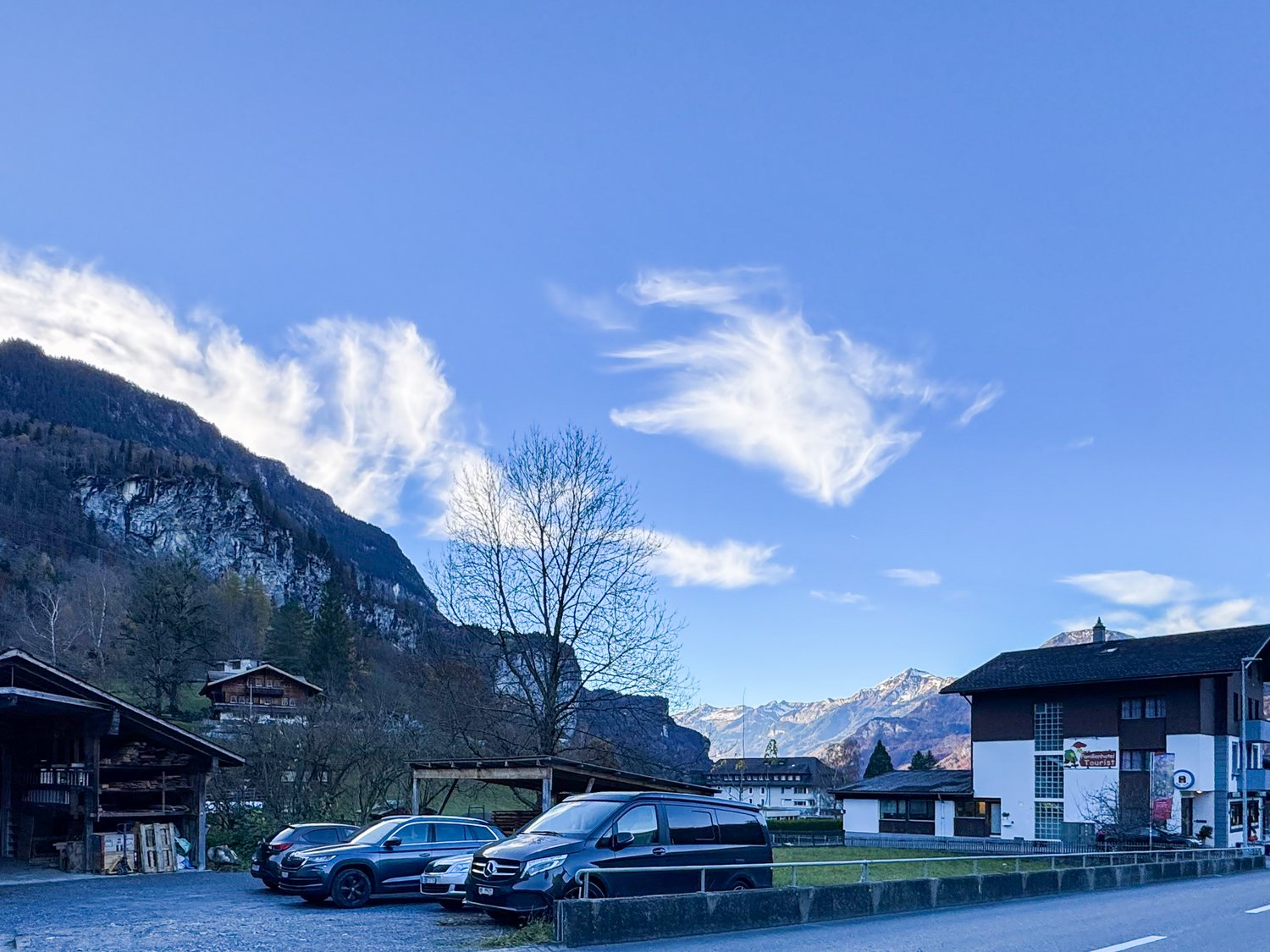 Mountainous area with a building, a shed, and a parking lot with several cars parked