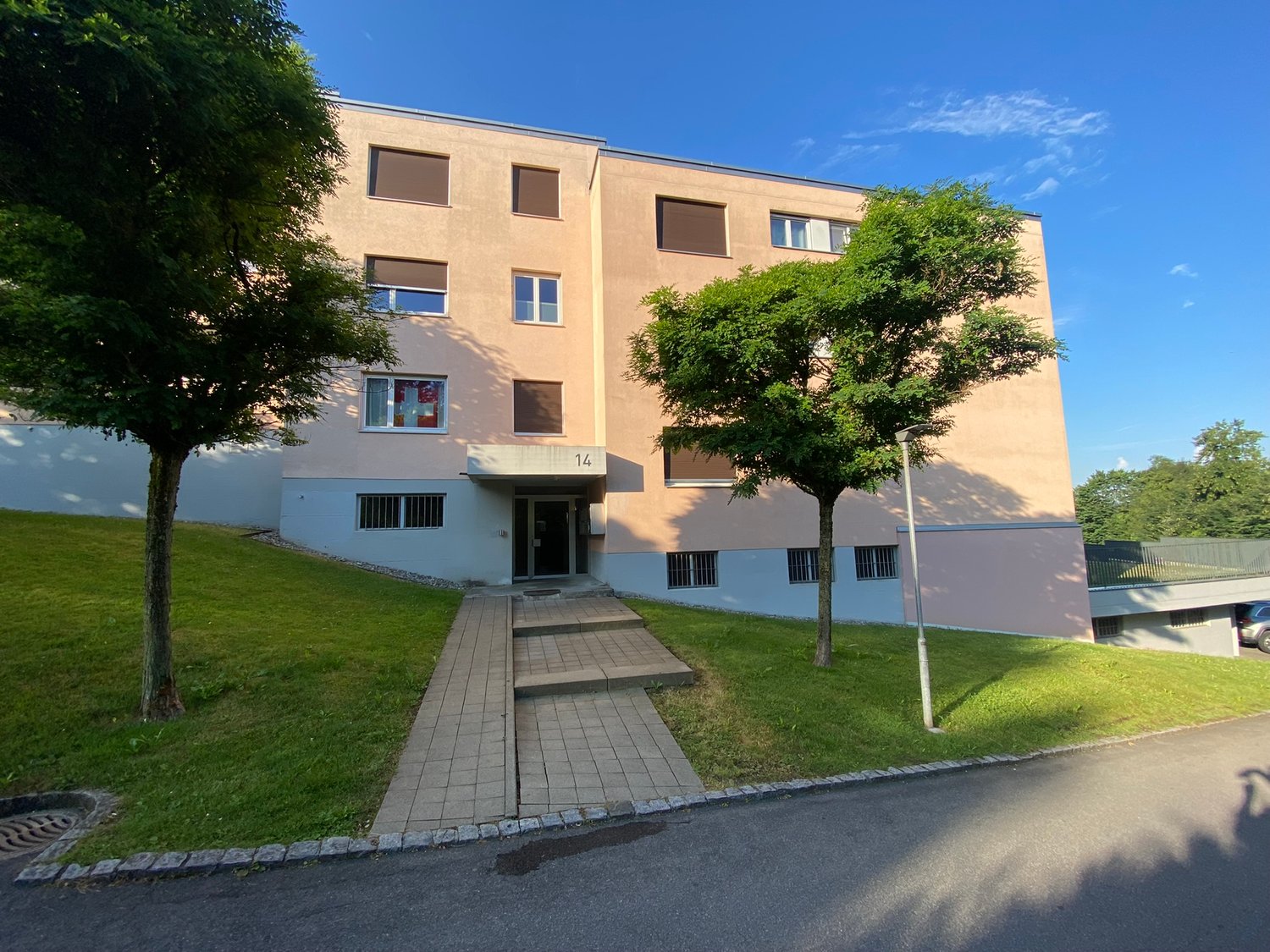3 story building, beige walls, windows with shutters, entrance with steps, car parked in garage