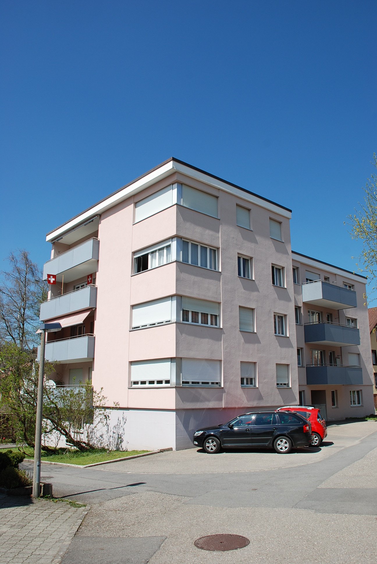 pink building, multiple balconies, two cars parked in front