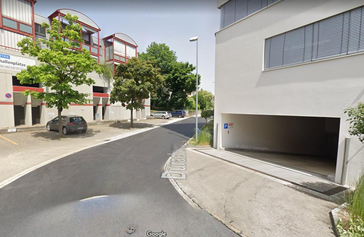 A street with a building on the left and a garage entrance on the right, with a car parked in front of the building.