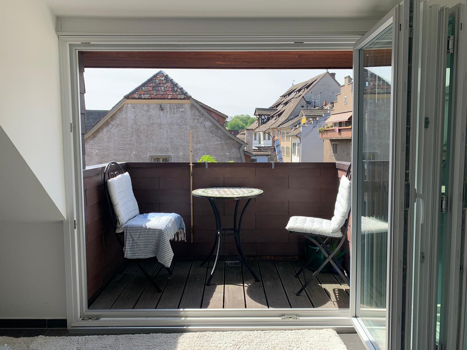 Balcony with table and chairs, wooden floor, open sliding doors, view of the city