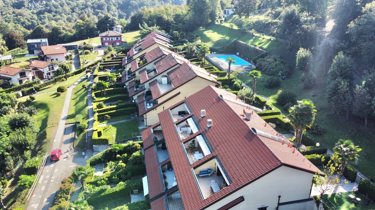 Multi-story apartment buildings with red tile roofs, surrounded by lush greenery and a swimming pool in the center of the complex