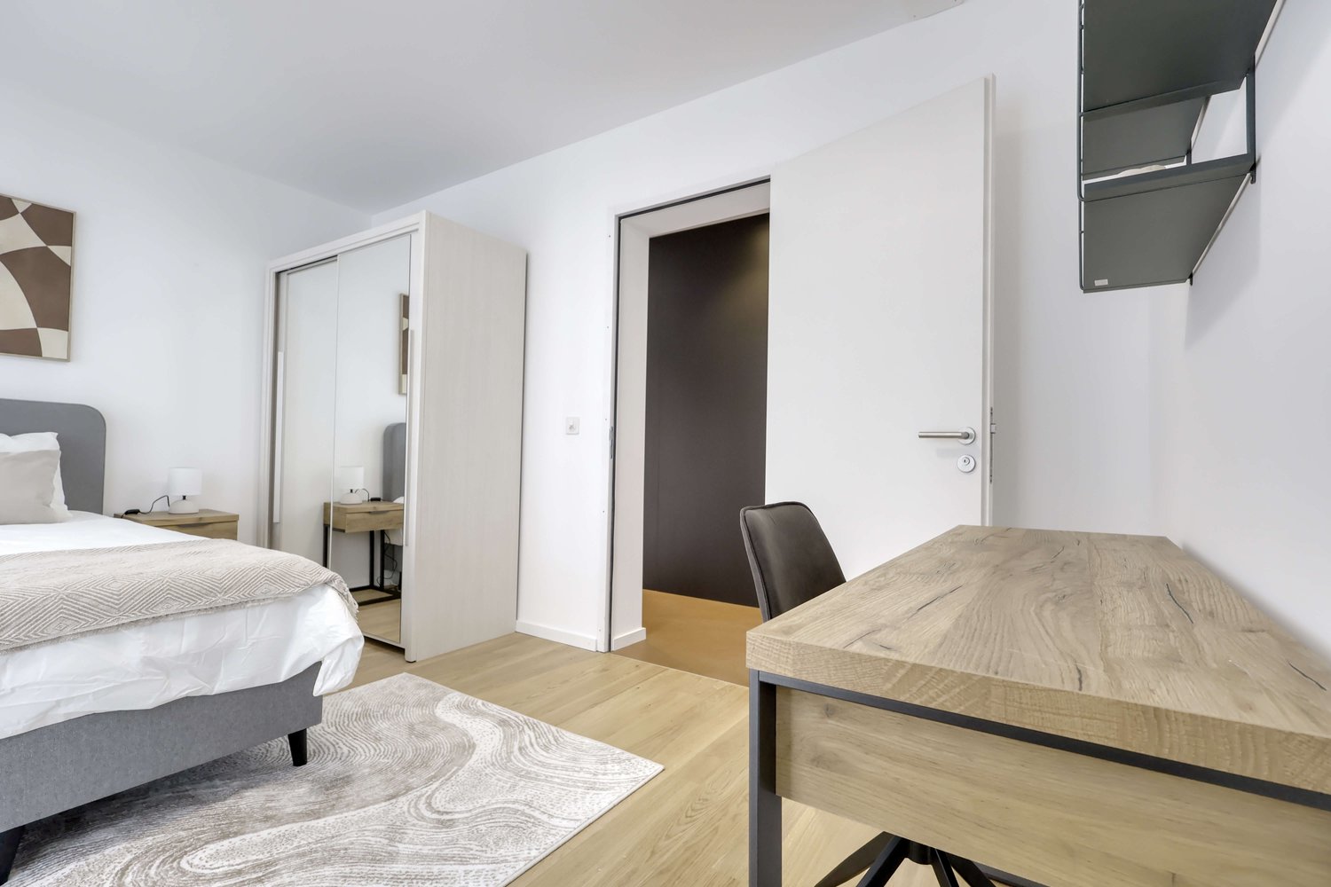 Bedroom with bed, desk, chair, rug, lamp, mirror, and artwork
