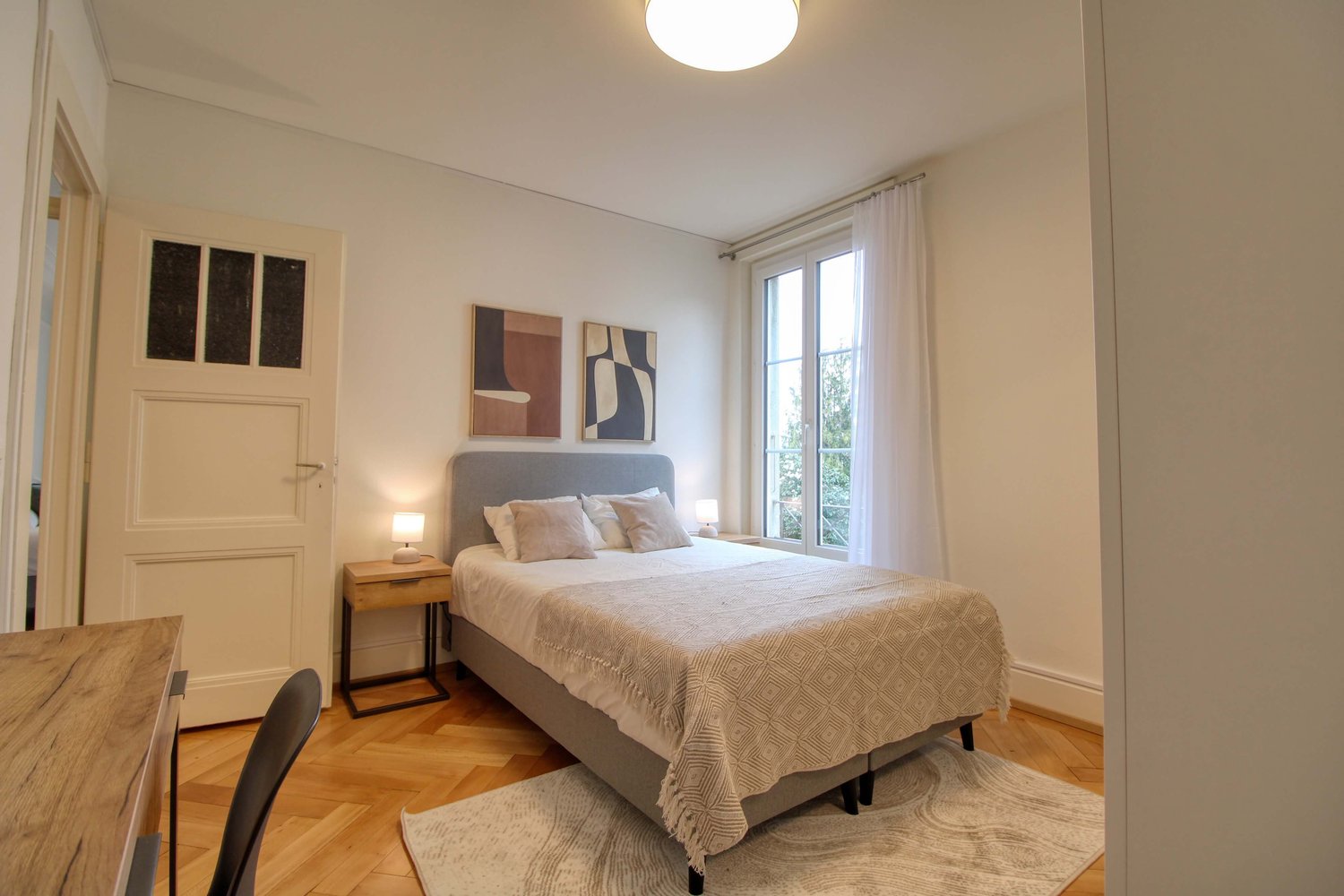 Bedroom with bed, nightstands, lamps, rug, and paintings on the wall