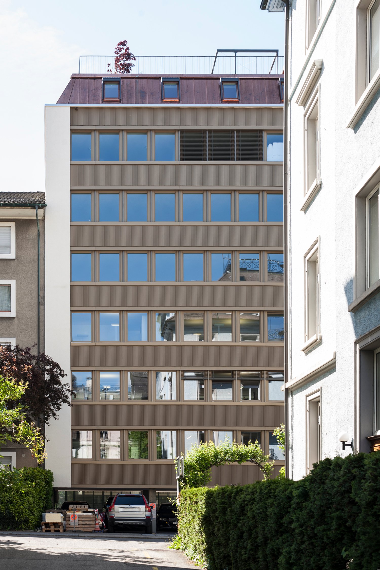 6 story building, glass windows, metal and wood exterior, cars parked at entrance, rooftop terrace
