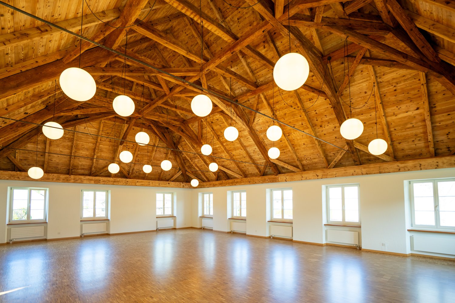 large open space, wooden floor, wooden ceiling, hanging lamps, windows
