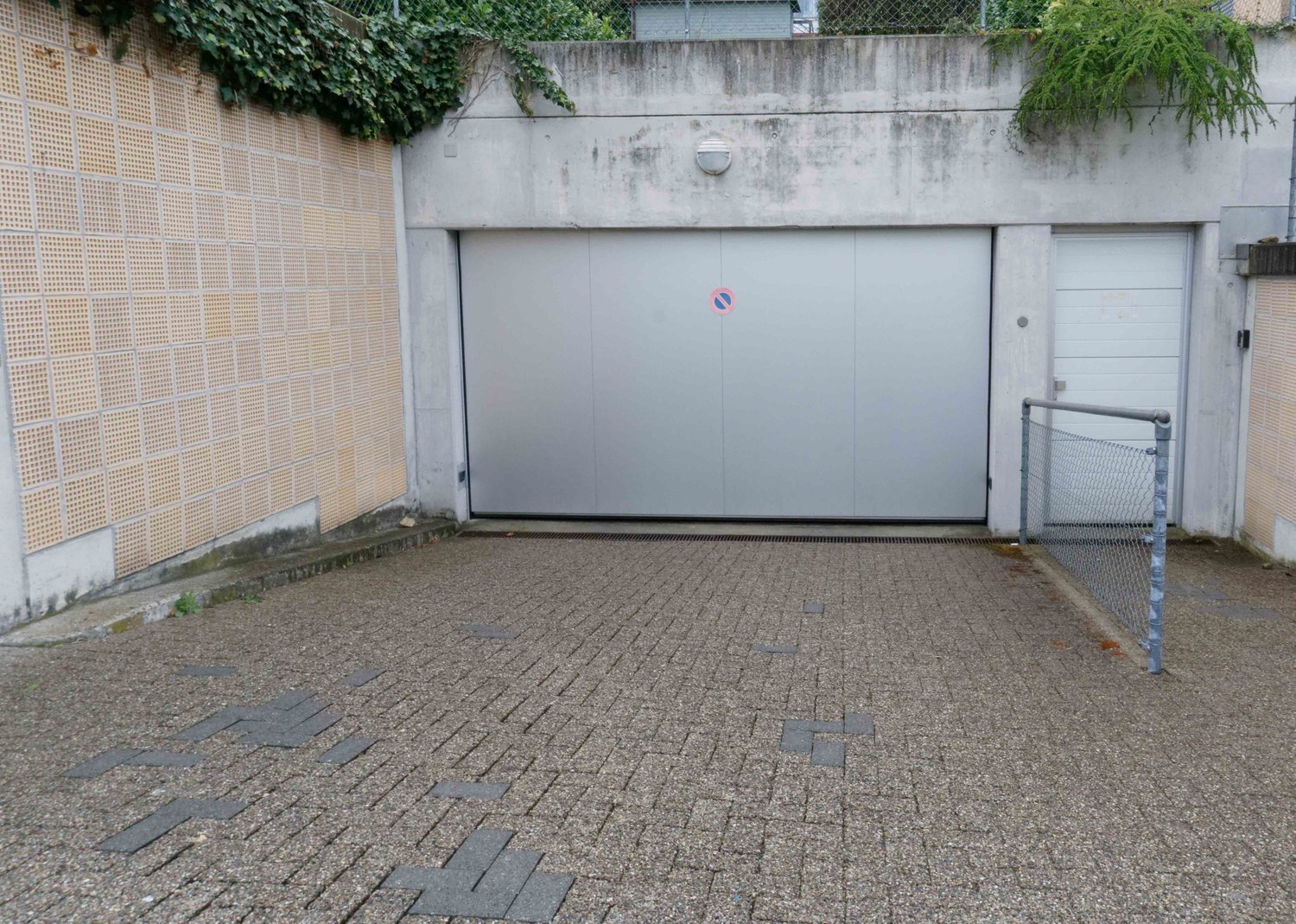 A concrete garage with two doors, one large and one small, and a small paved area in front.