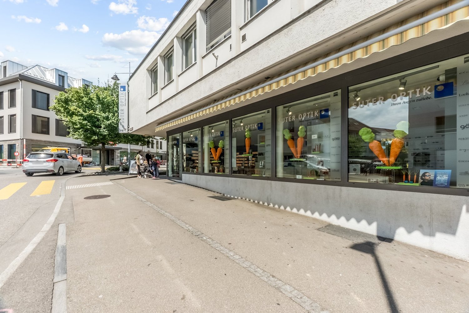 2-story commercial building with an optician shop on the ground floor, awnings, and parked cars on the street in front of the building