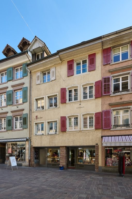 2-story building, red shutters, large windows, ground floor storefronts, cobblestone street