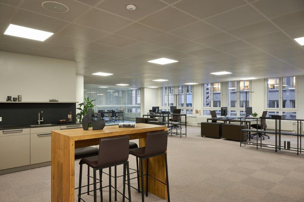 Large open-plan office space with modern furniture and amenities. The space features a kitchen area with a dishwasher, as well as multiple workstations and a communal dining/meeting table.
