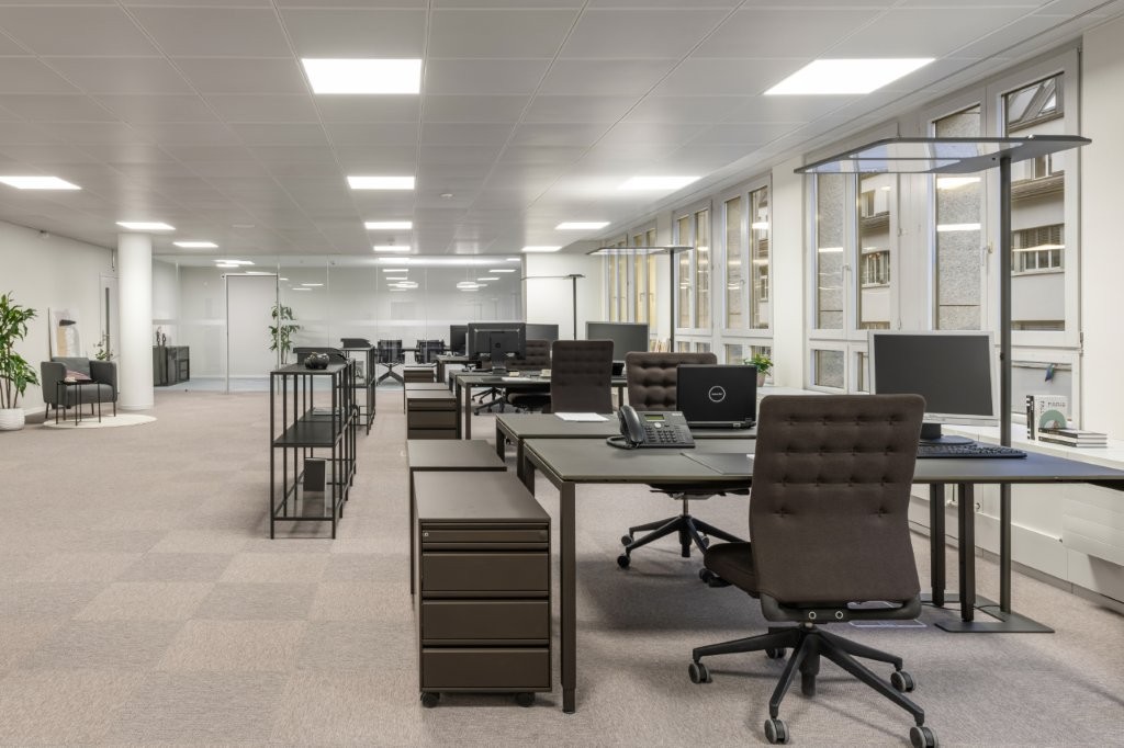 Modern office space with contemporary furnishings, white walls, large windows, beige carpeting, and various office equipment