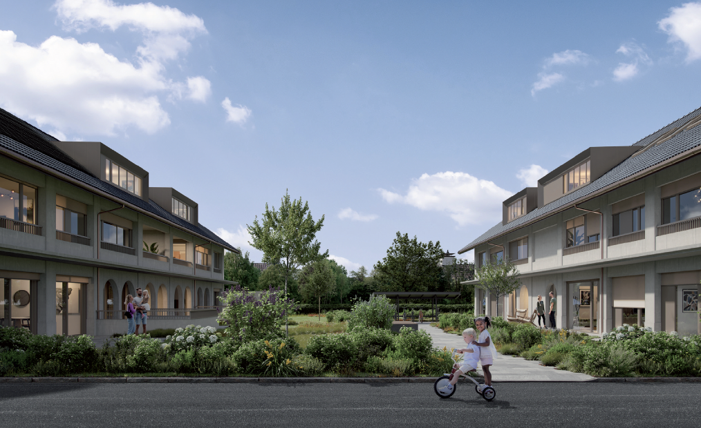 The image shows a residential complex with multiple two-story buildings. The buildings have balconies and large windows, and are surrounded by a well-landscaped garden area with trees and walkways. There are people visible in the garden, including a perso