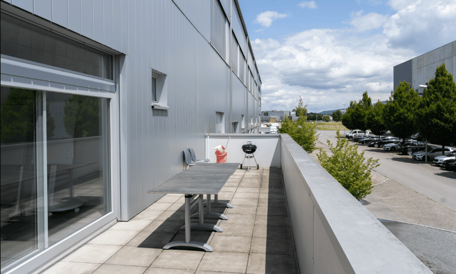 Outdoor balcony with table, chairs, grill and trees.