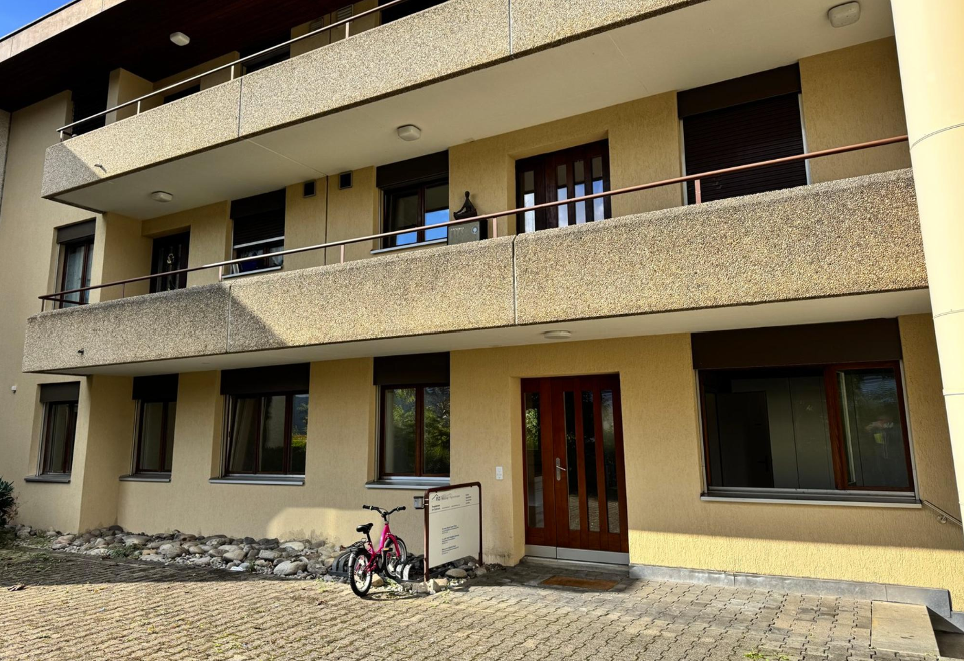 Two-story building, with multiple balconies, front door, pink bicycle parked.