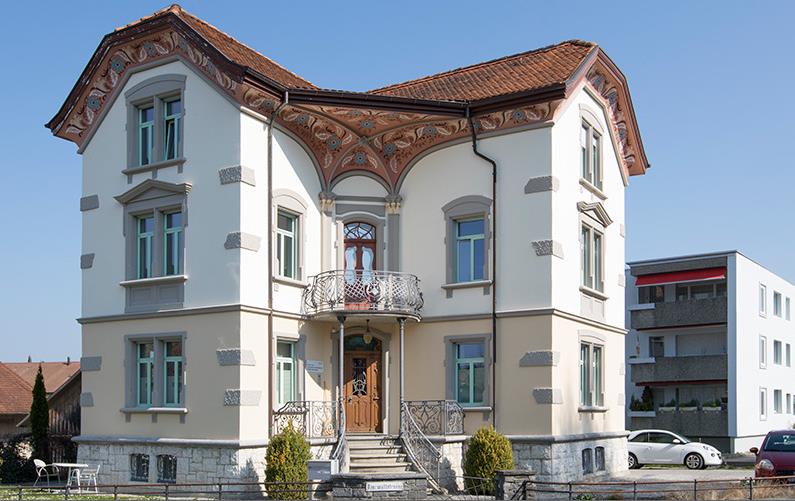 white house, brown roof, multiple windows, large entrance with steps, balcony