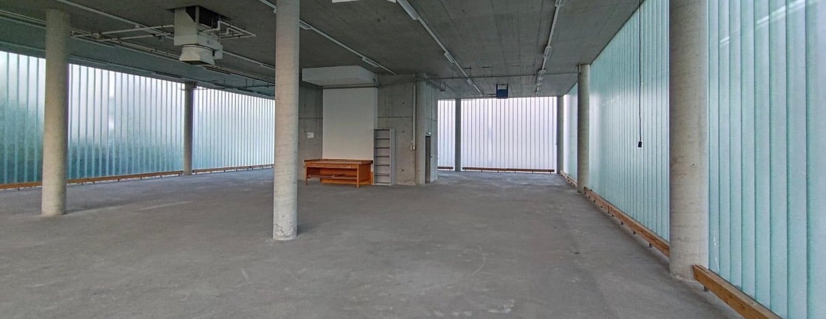 Empty concrete room, concrete flooring, large glass windows, small wooden desk.