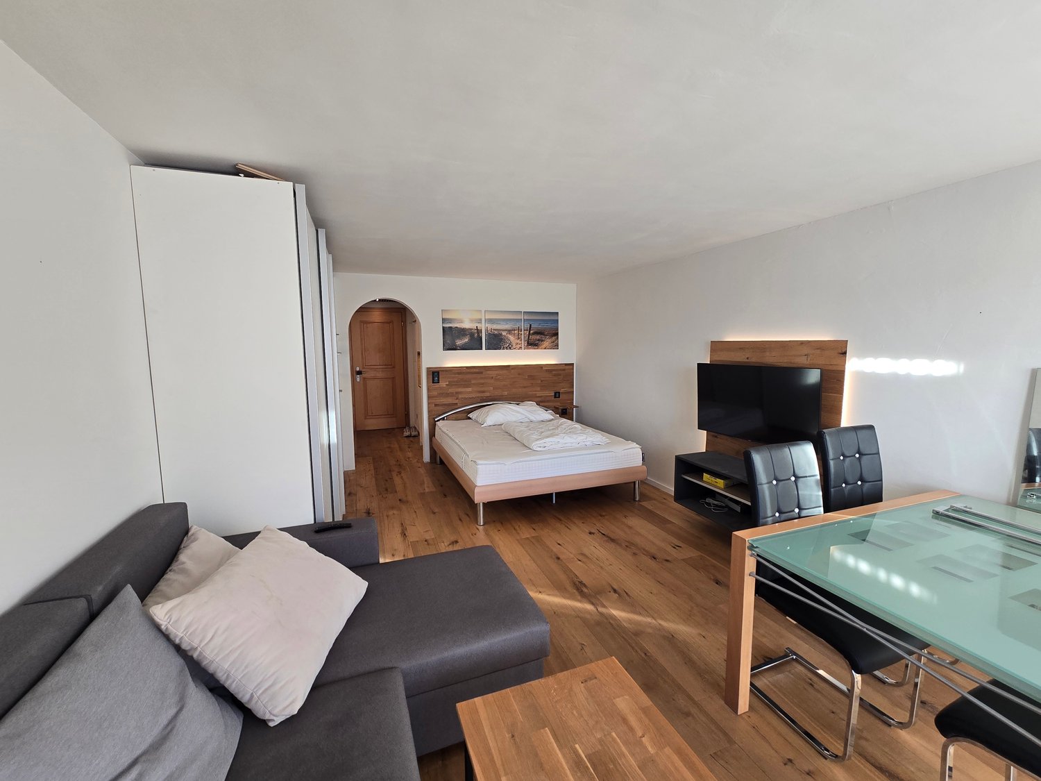 A room with a bed, couch, TV, dining table, and chairs.