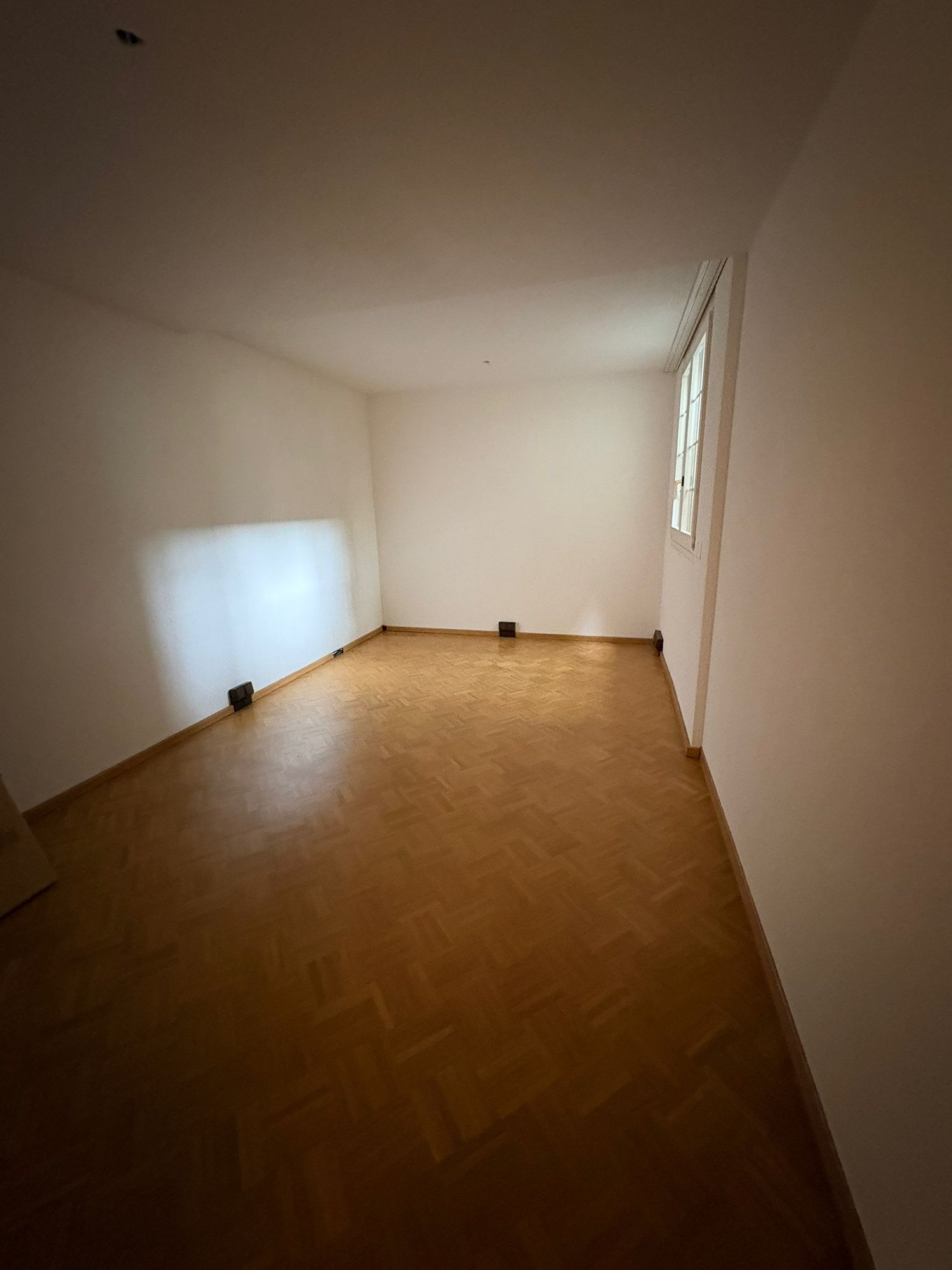 an empty room with wooden floor, white walls, and a window