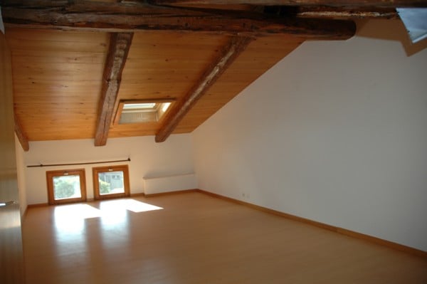 Empty room with wooden floor, wooden ceiling, two windows, and white walls.