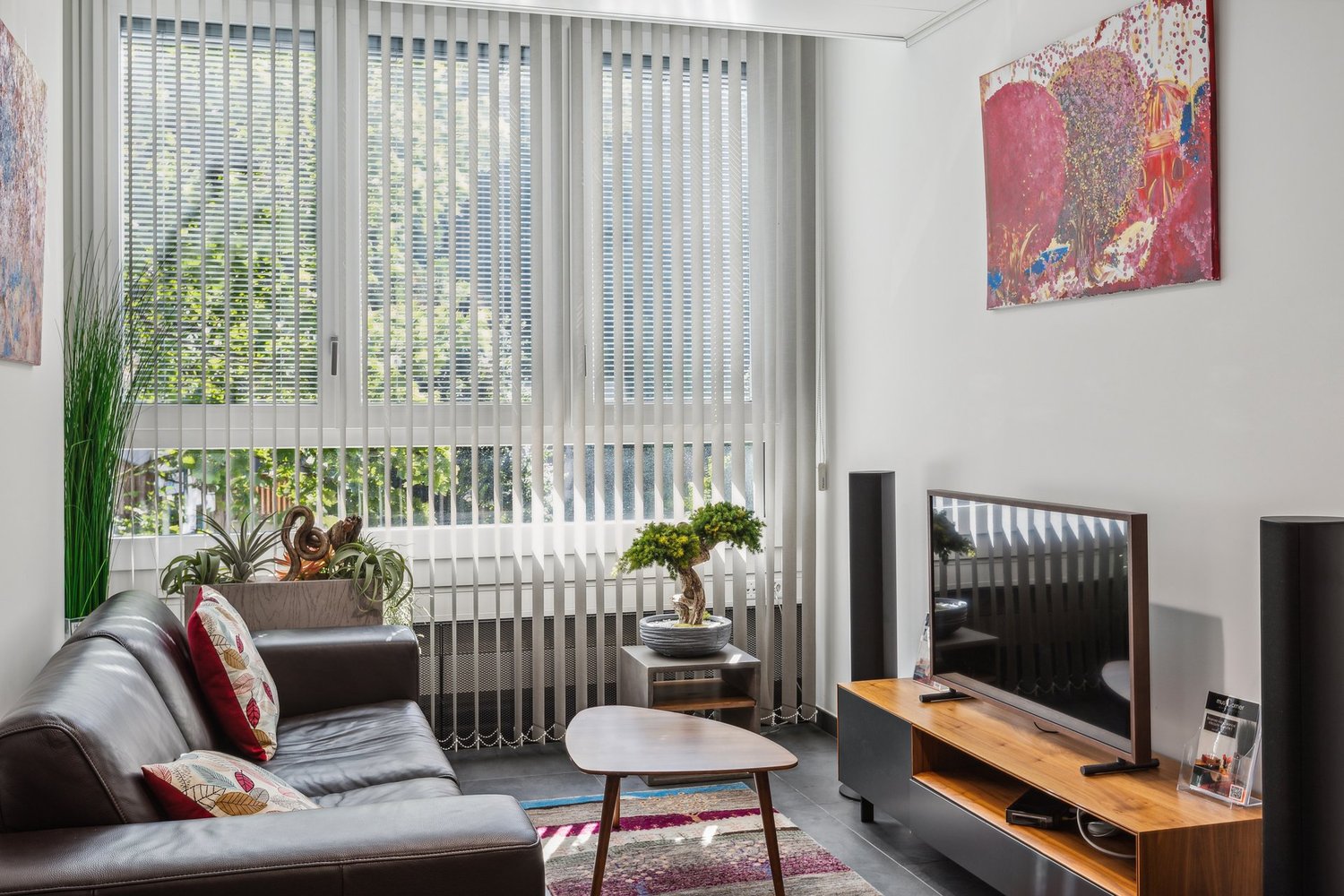 modern decor, brown sofa, coffee table, wall-mounted TV, wooden TV stand, floor lamps, decorative items, large window with vertical blinds